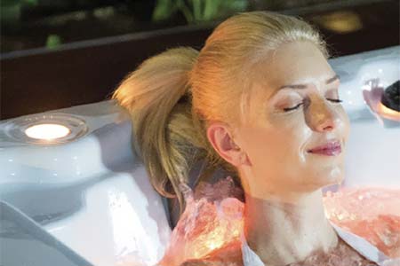 blonde woman enjoying a warm hot tub soak in the evening.