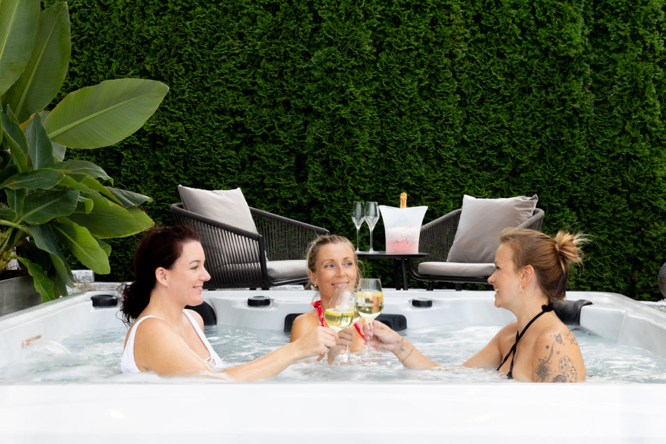 Women drinking white wine and toasting inside the hot tub in a garden.