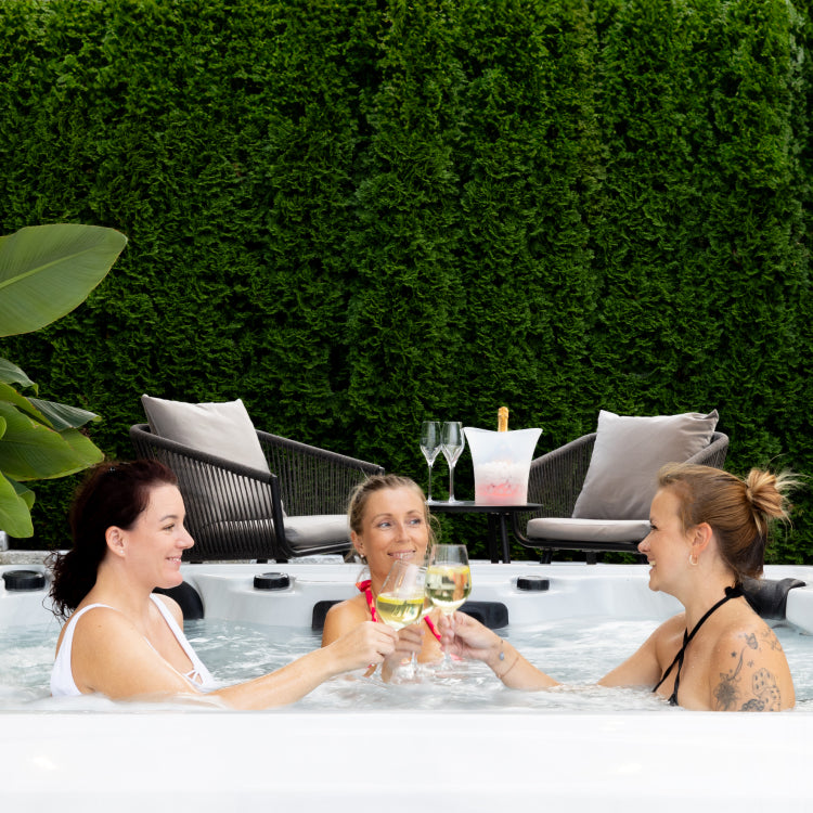 Women drinking white wine and toasting inside the hot tub in a garden.